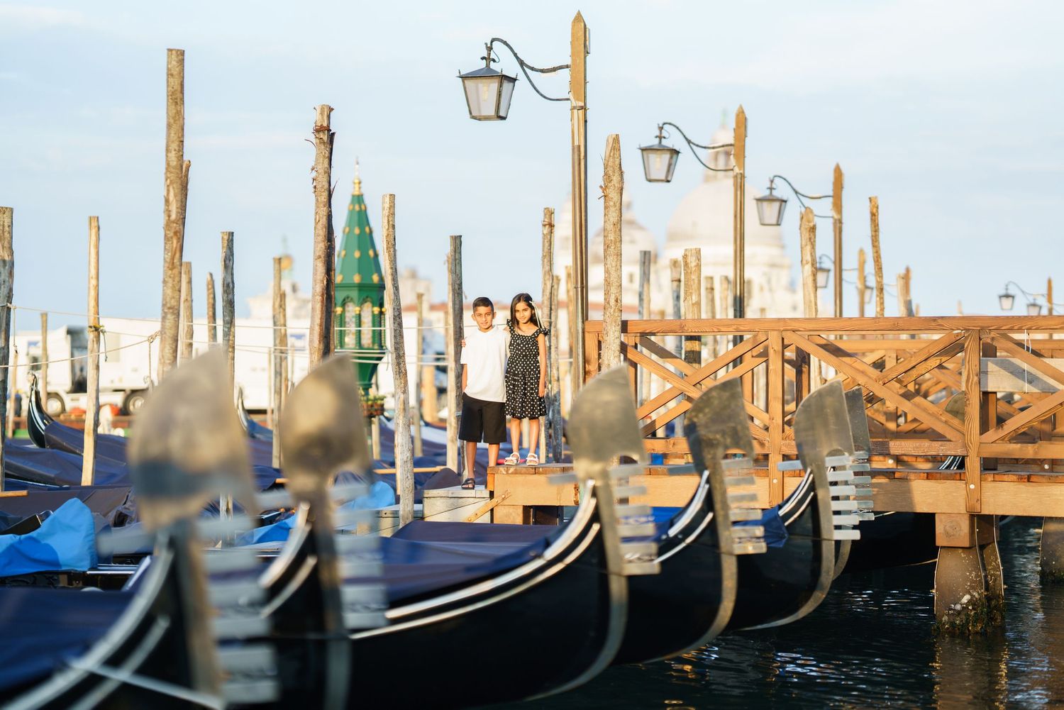 Couple standing on a wooden dock surrounded by gondolas in Venice, Italy at golden hour.