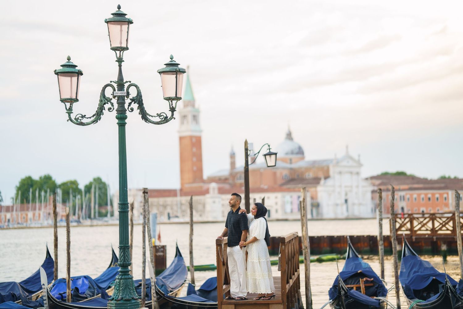 Couple embracing near gondolas on Venice Grand Canal with San Giorgio Maggiore church in background.