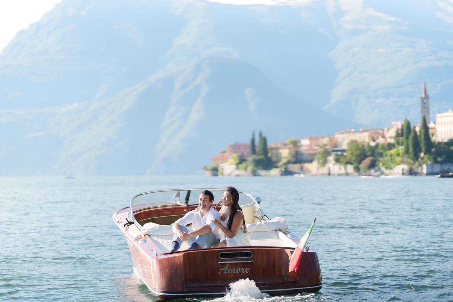 Couple enjoying a romantic boat ride on Lake Como with scenic mountains and Italian village in the background.