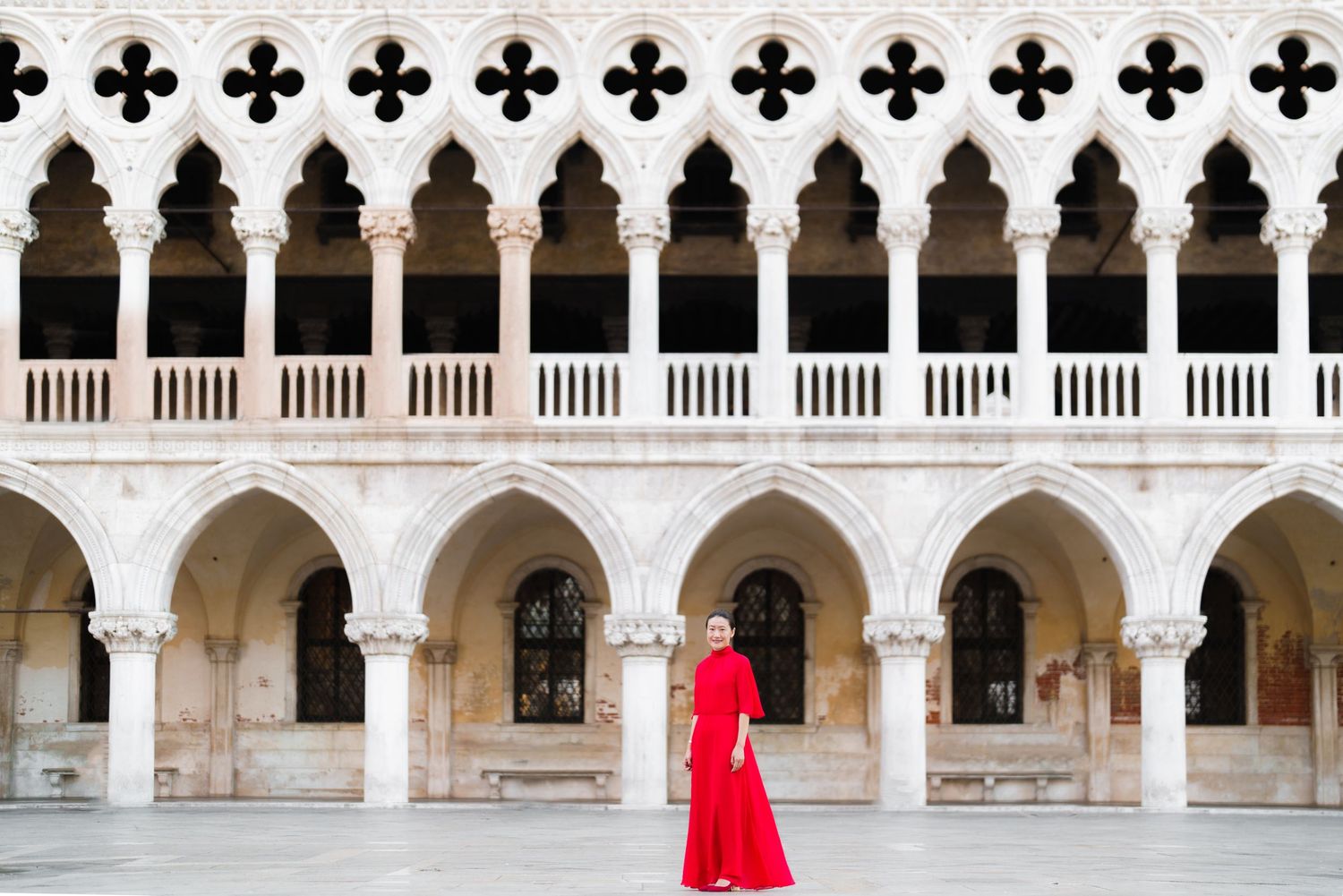 Woman in red dress standing in the ornate courtyard of the Doge's Palace in Venice, Italy.