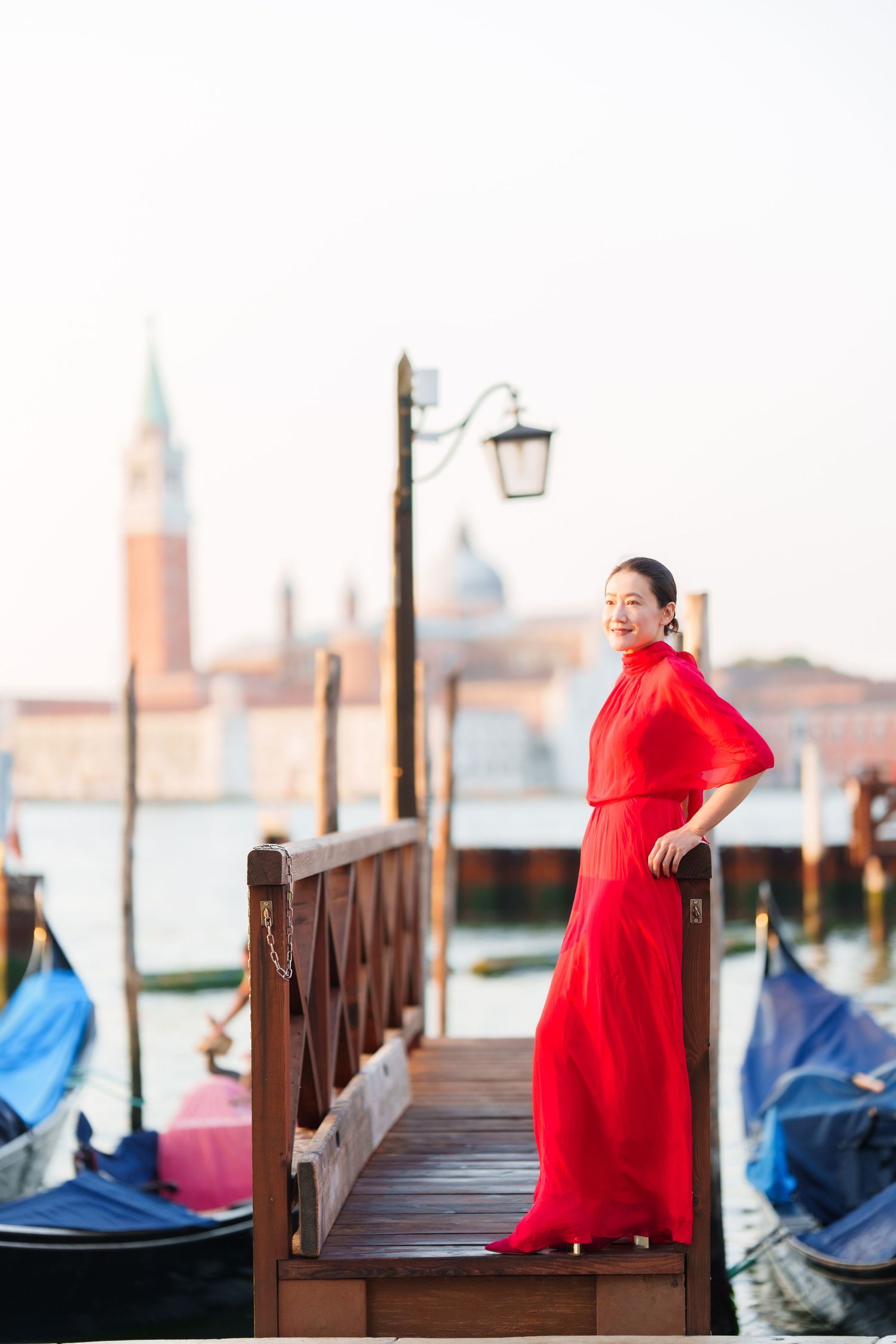 Woman in red dress posing on Venice dock with gondolas and San Giorgio Maggiore island in background.