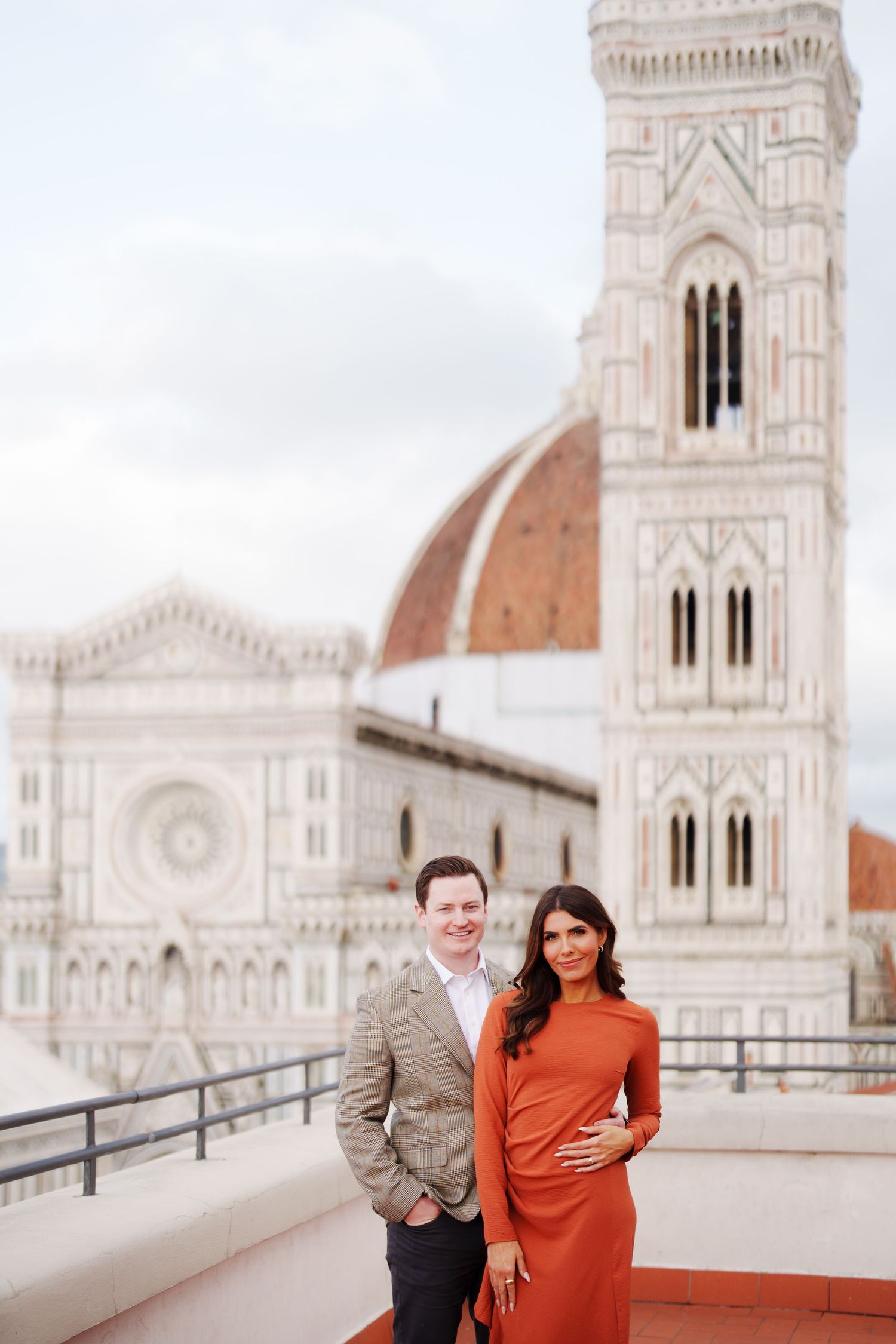 Couple posing on a rooftop terrace with Florence Cathedral dome and Giotto's Campanile in background.