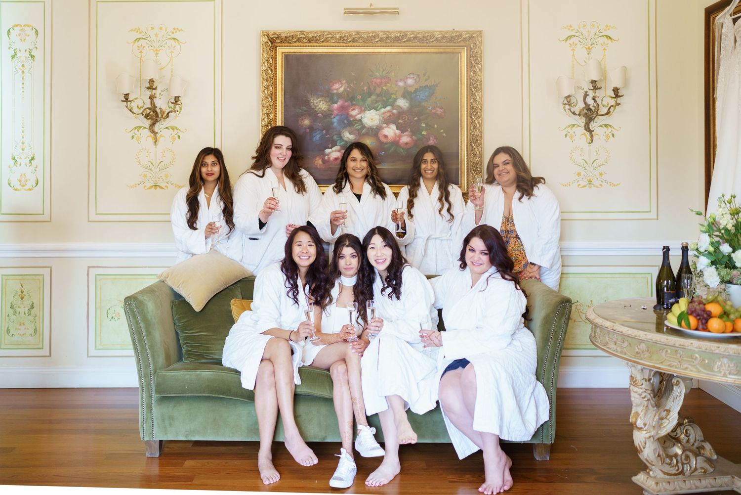 Group photo in white outfits seated on green velvet sofa in ornate room with gold frames.