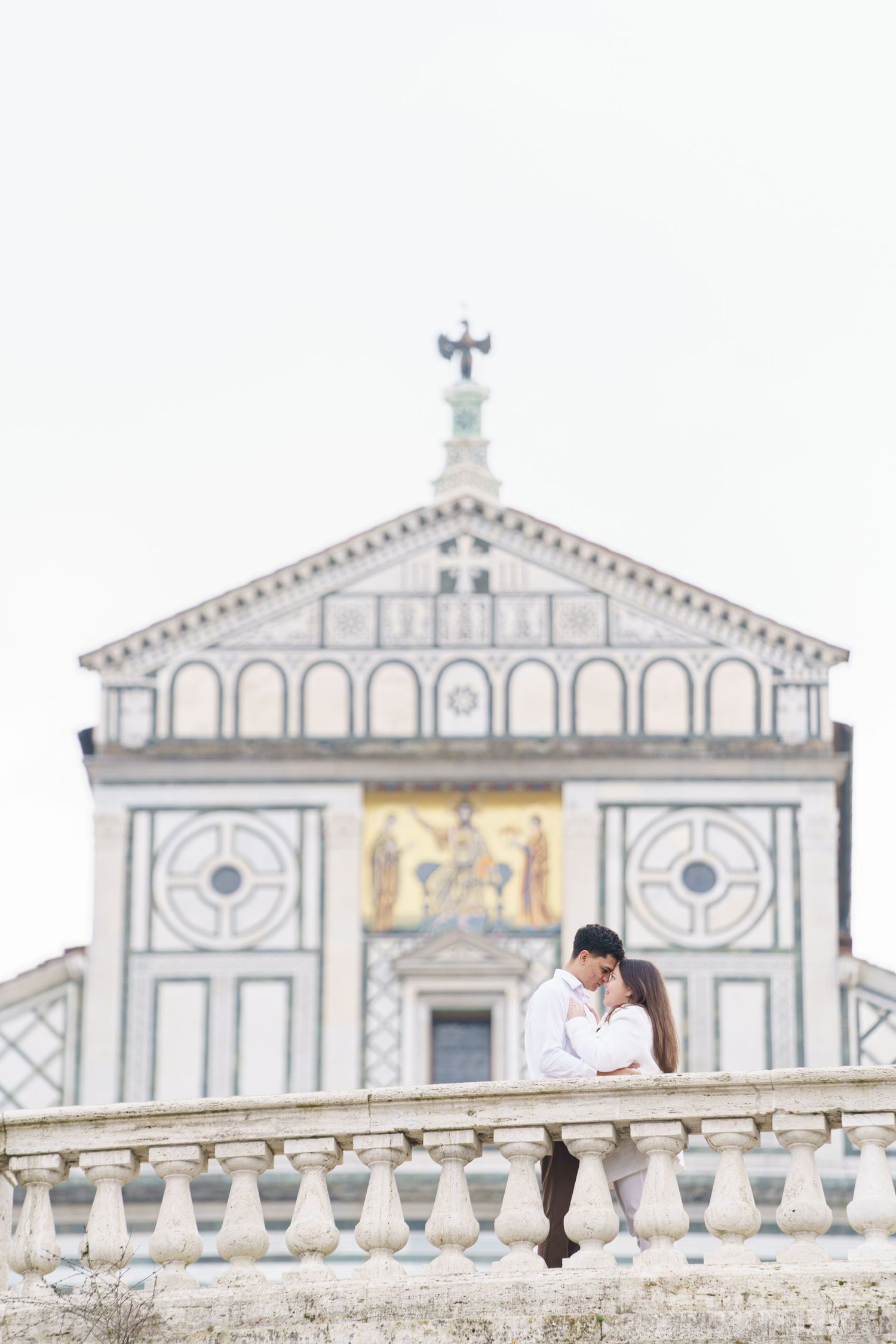 Intimate portrait against the white marble facade of San Miniato al Monte church in Florence.
