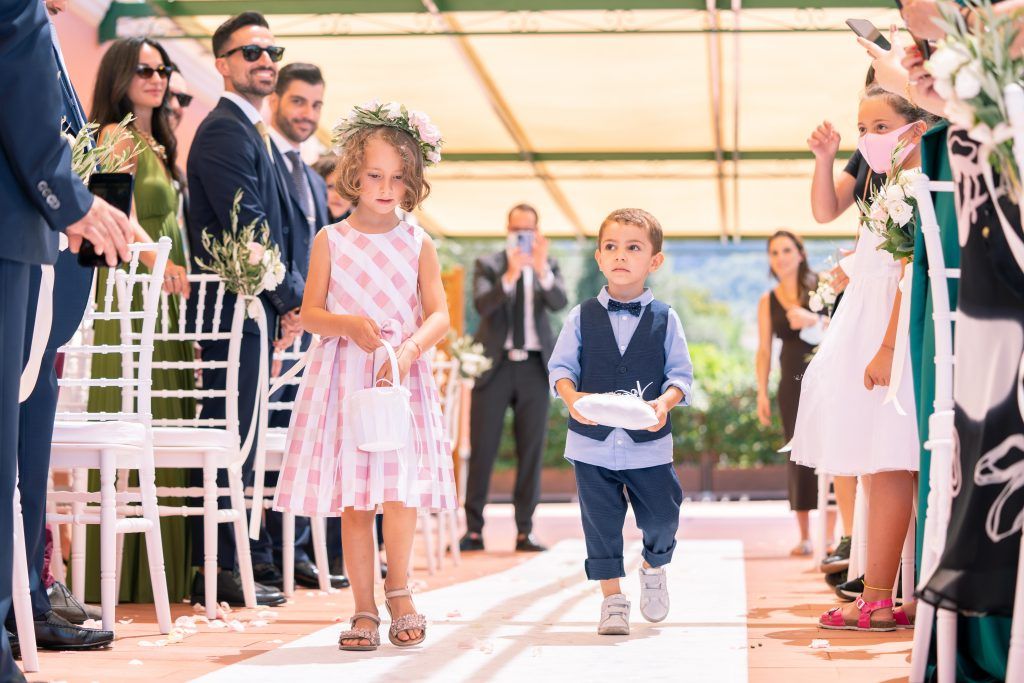 Wedding guests and bridal party gather on a sunny outdoor terrace during ceremony.