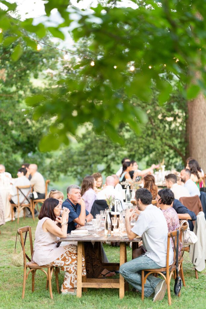 Outdoor wedding reception with wooden chairs and tables arranged under green tree canopy.