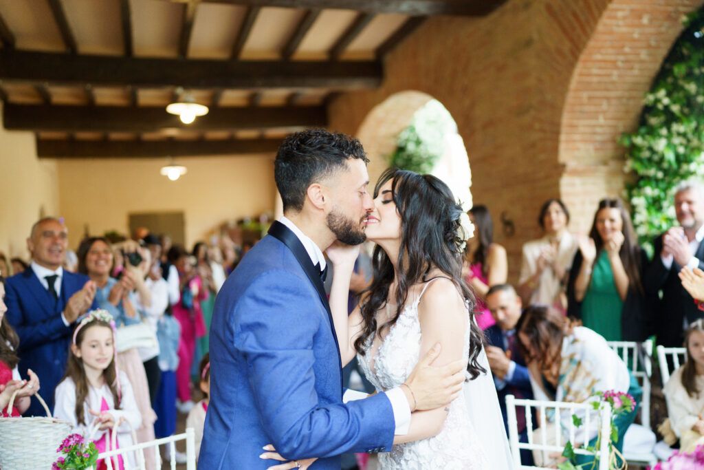 Wedding guests gather in a rustic venue with exposed wooden beams and brick walls.