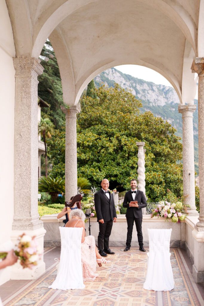 Wedding party gathered under ornate white archways with mountain views in the background.