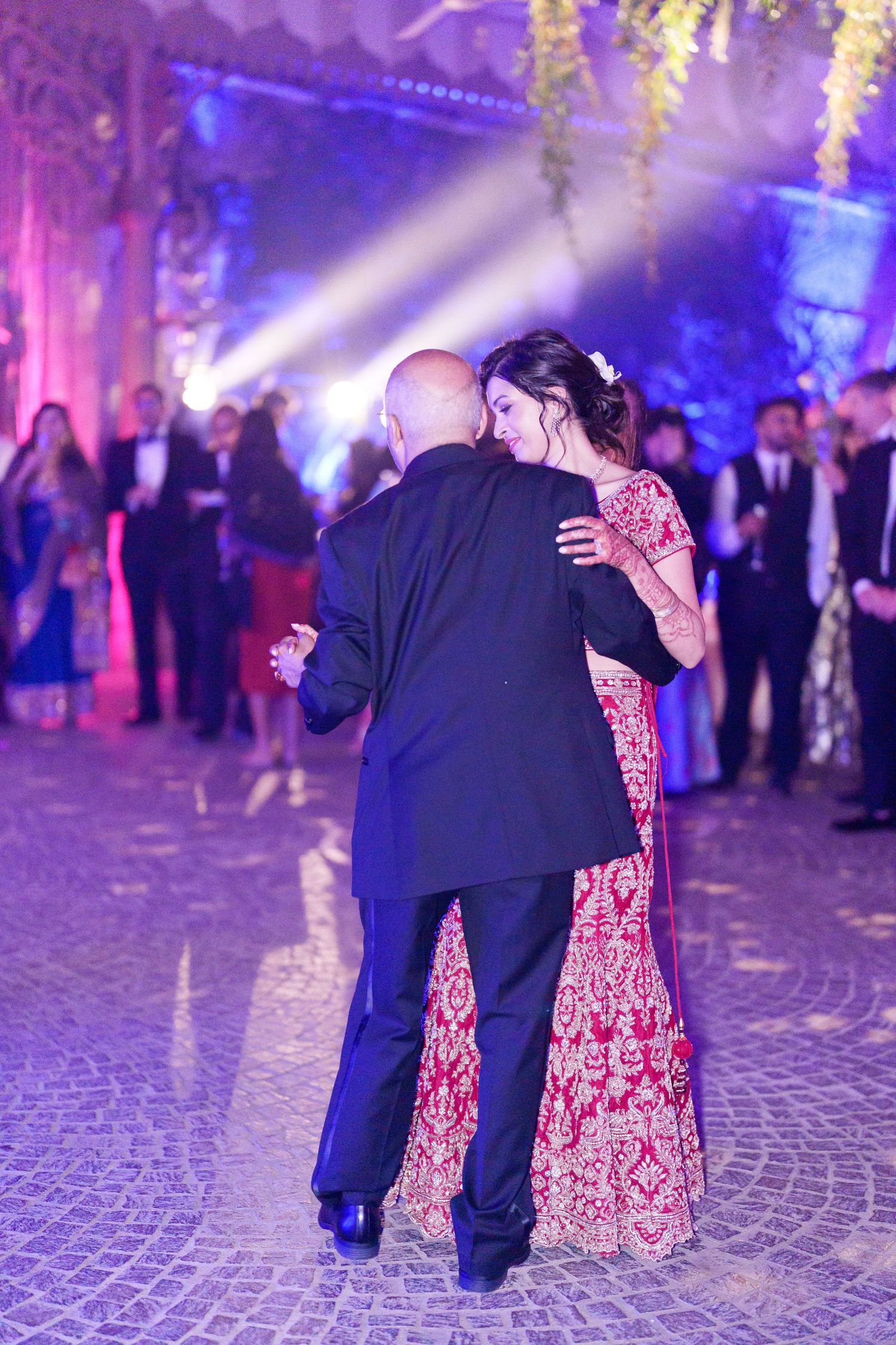 Couples share an intimate dance moment under dramatic purple and blue lighting at an elegant reception.
