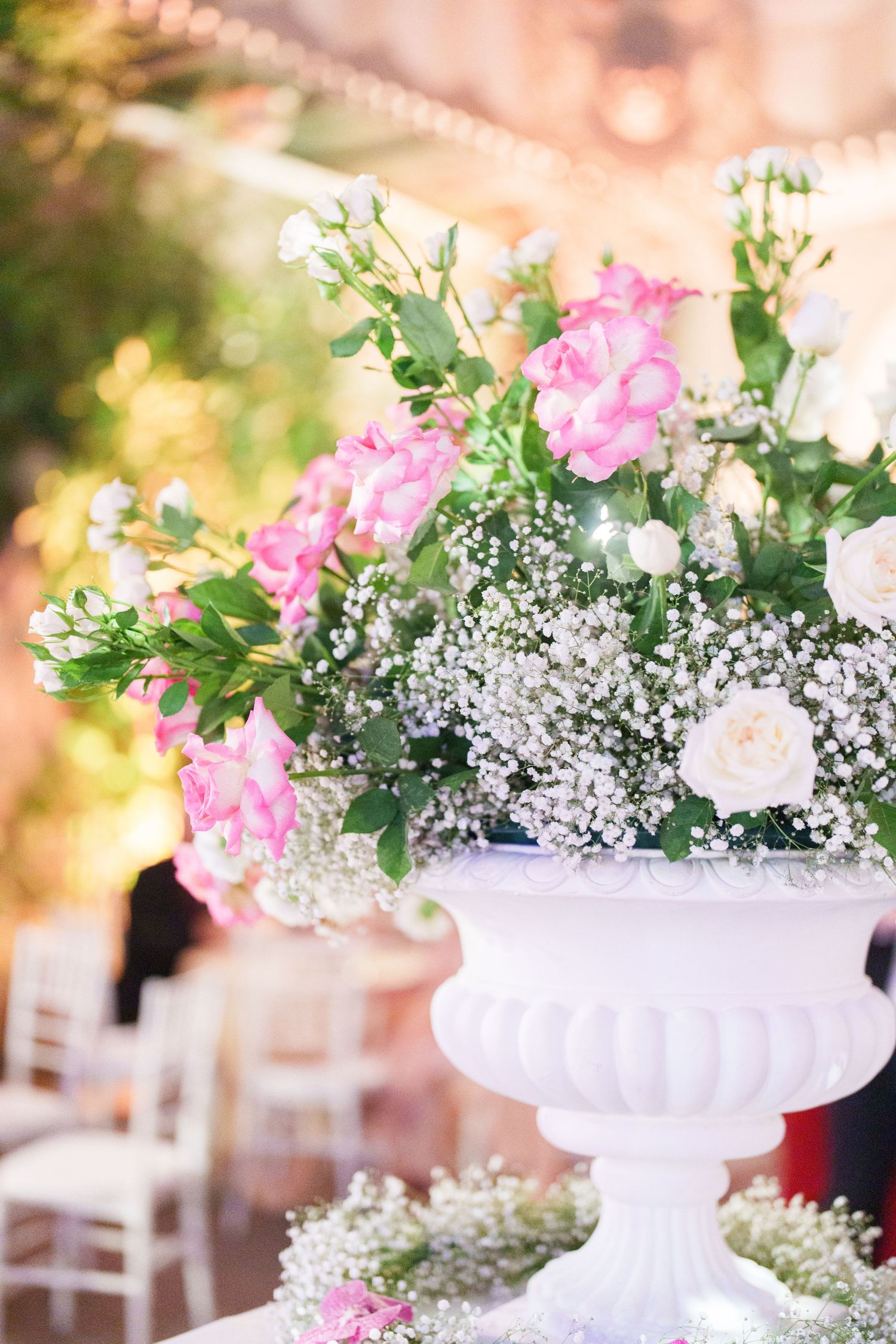 White ceramic urns filled with pink roses and baby's breath create elegant wedding centerpieces.