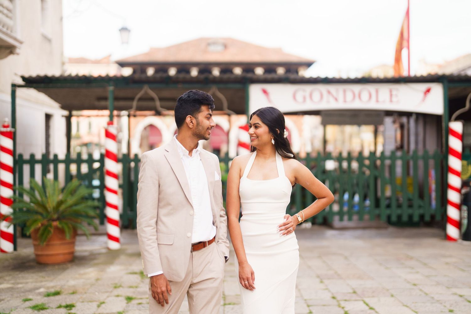 Bride and groom walk hand in hand along a palm-lined pathway in their elegant white wedding attire.