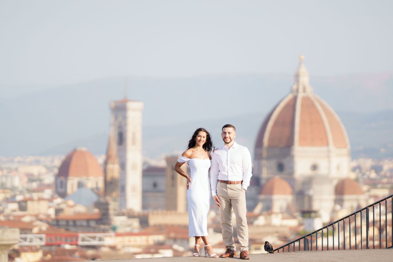 A couple stands on a scenic overlook with Florence's iconic Duomo cathedral and cityscape in the background.