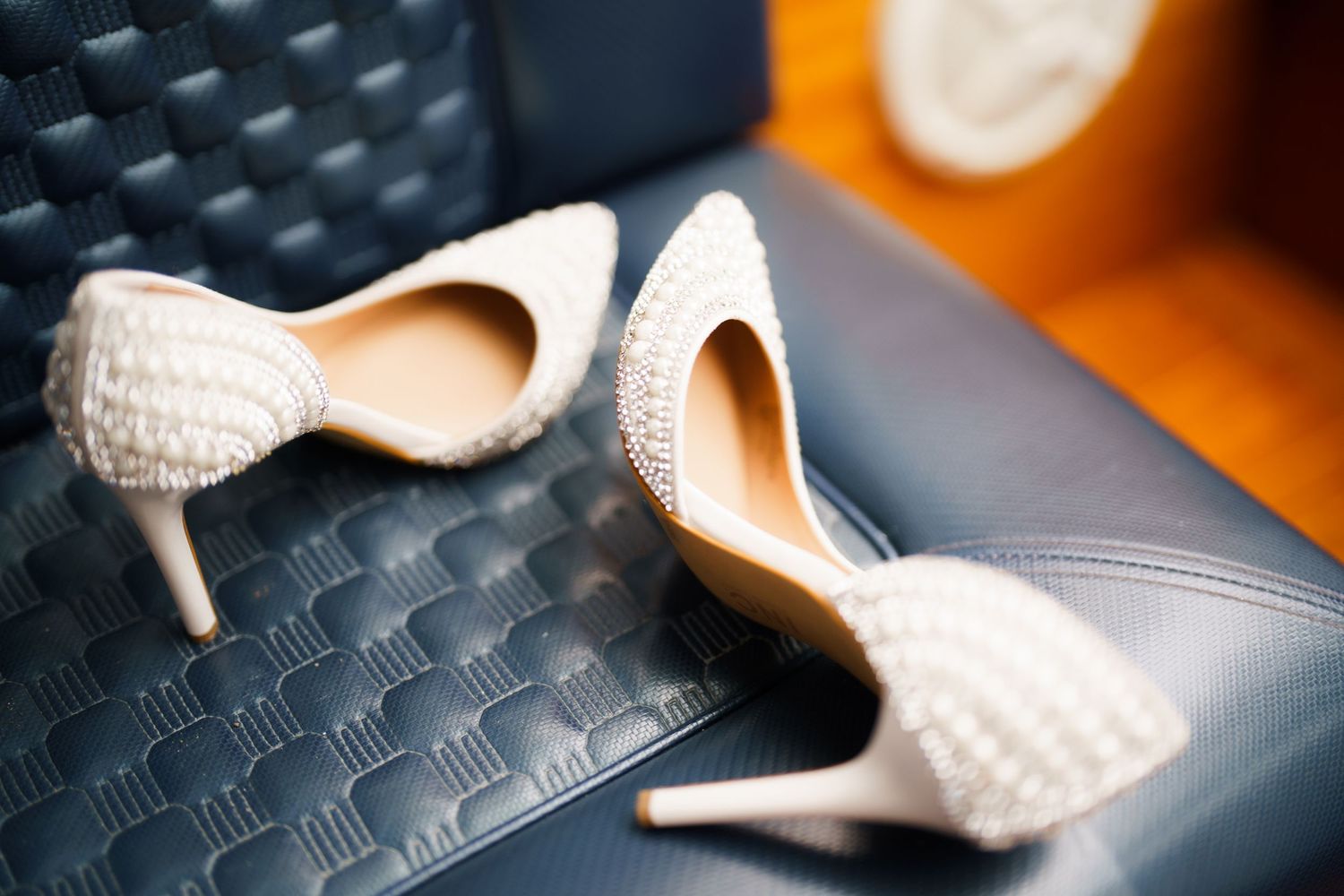Elegant white textured bridal heels on a dark leather surface with soft focus background.