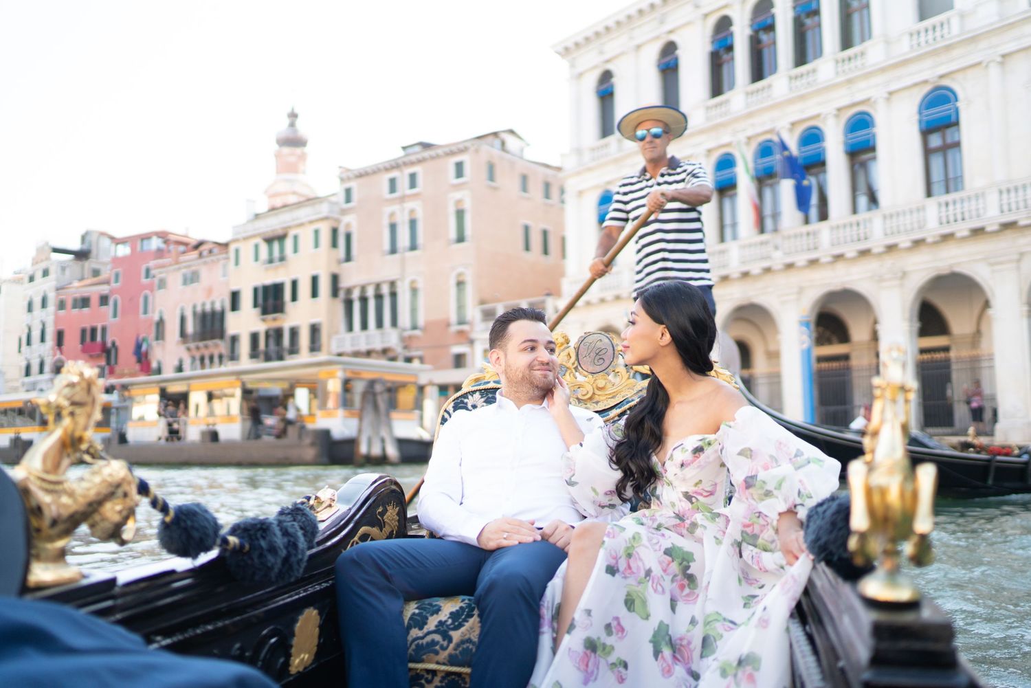 A romantic couple enjoys a gondola ride through the scenic canals of Venice, Italy with historic buildings in view.