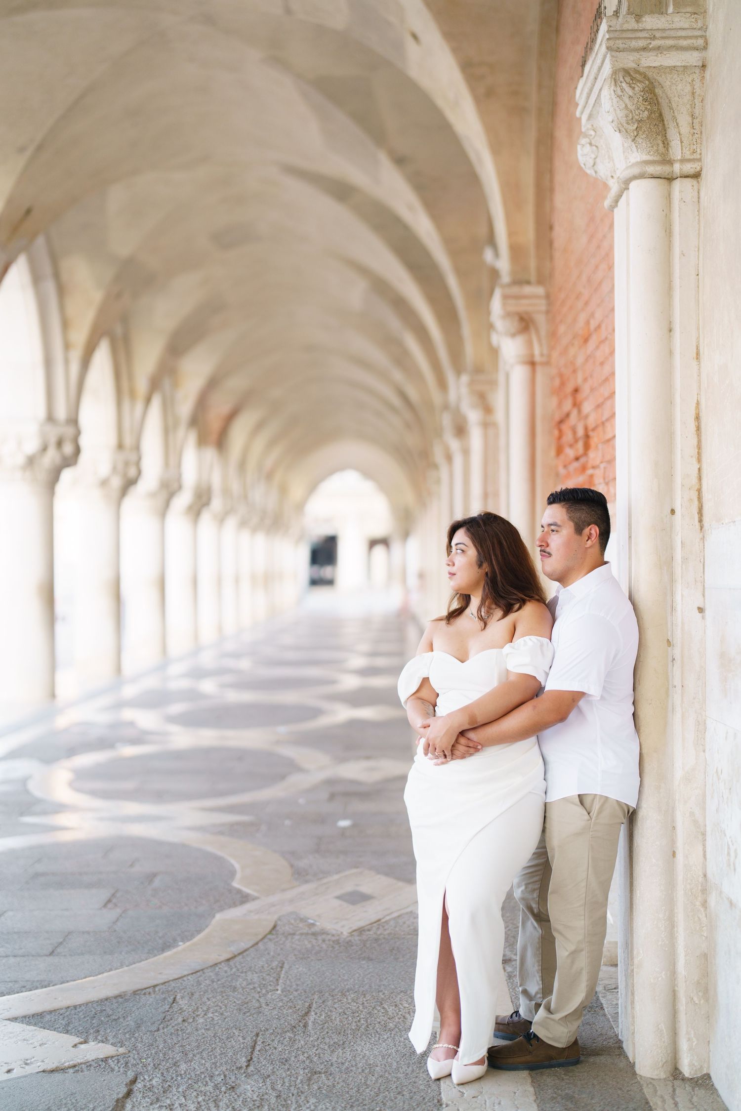 A couple shares a romantic moment under the arched colonnade of a historic building.