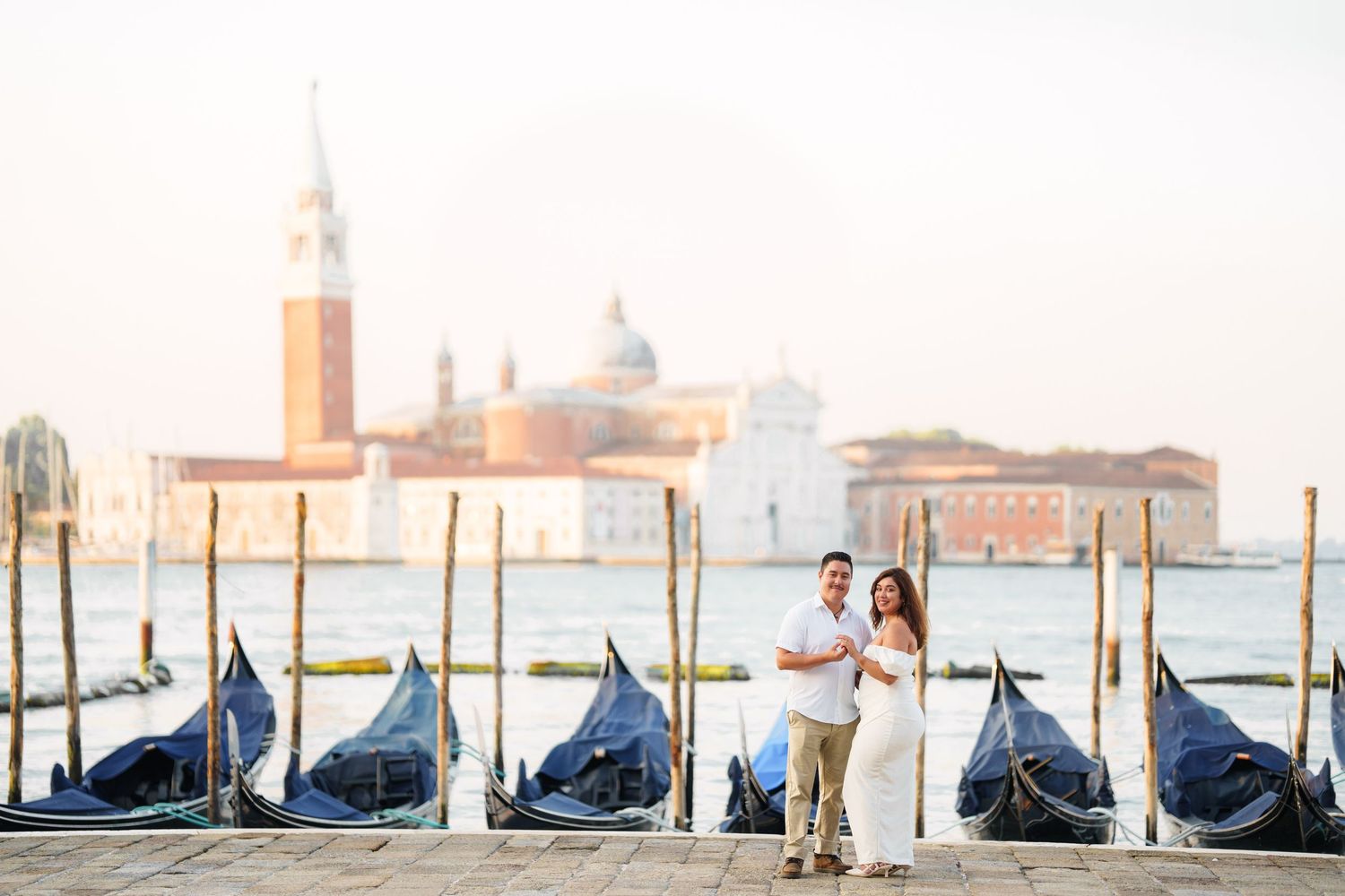 Row of traditional gondolas moored along Venice waterfront with San Giorgio Maggiore church in the background.