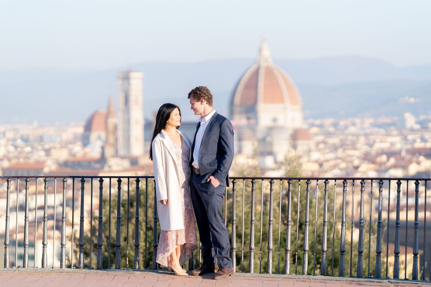 Couple standing at scenic viewpoint overlooking Florence Italy with Duomo cathedral dome visible in background.