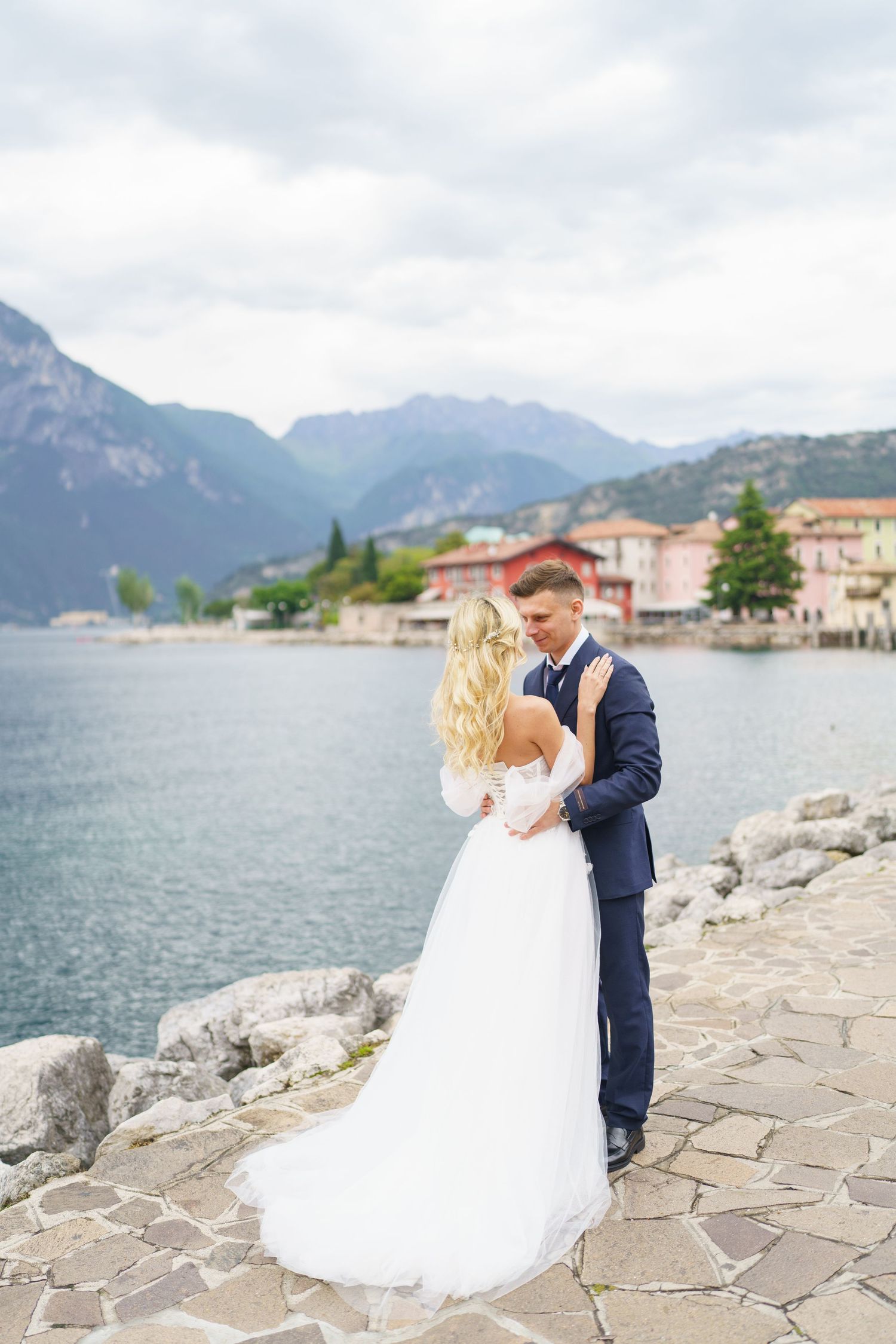 A romantic couple shares intimate moments along a scenic lakeside with mountains in the background in Lake Como, Italy.