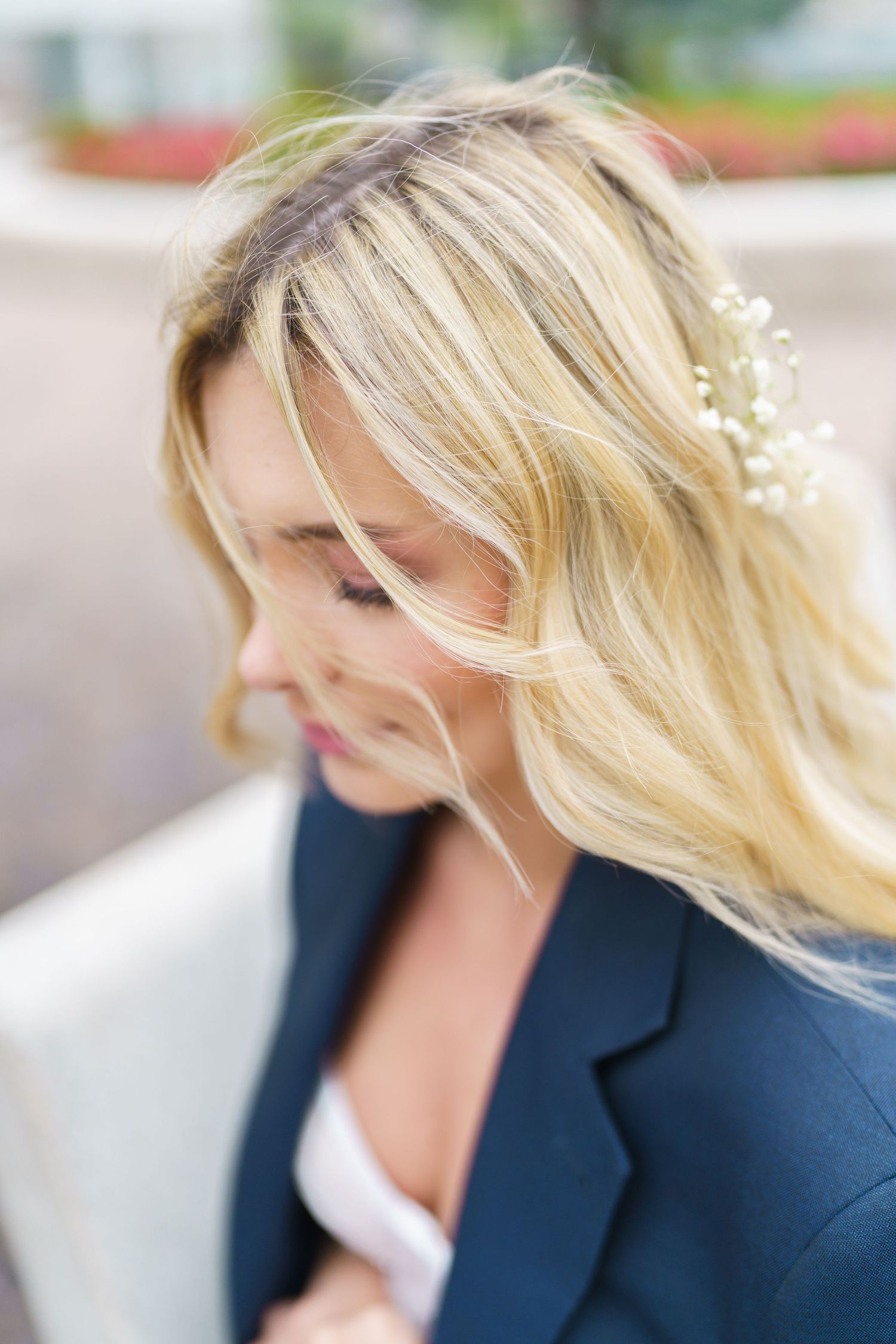 Professional woman in navy blazer with blonde hair blowing in wind against blurred outdoor background.