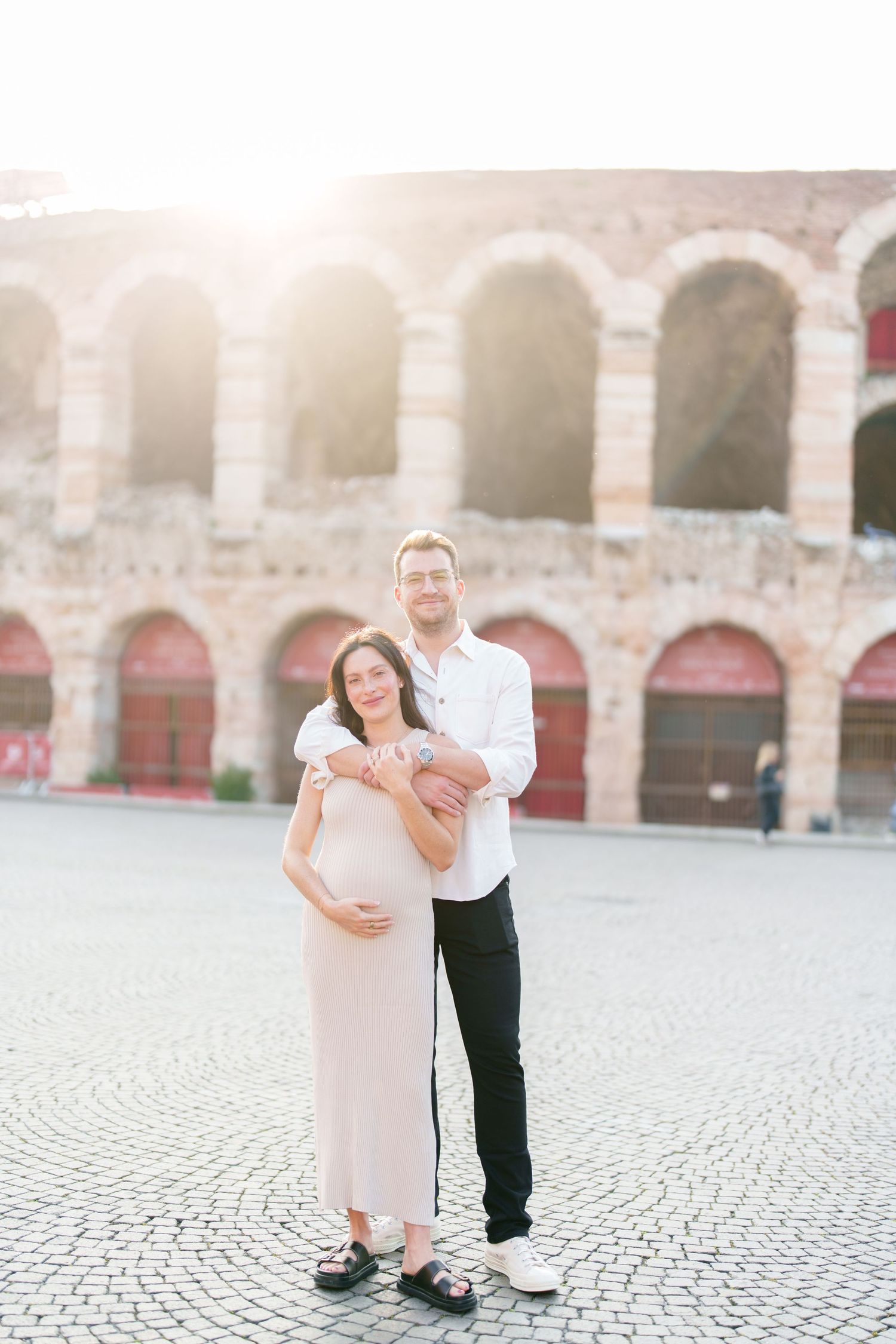 A couple shares a romantic moment together on a cobblestone plaza with arched architecture in the background.