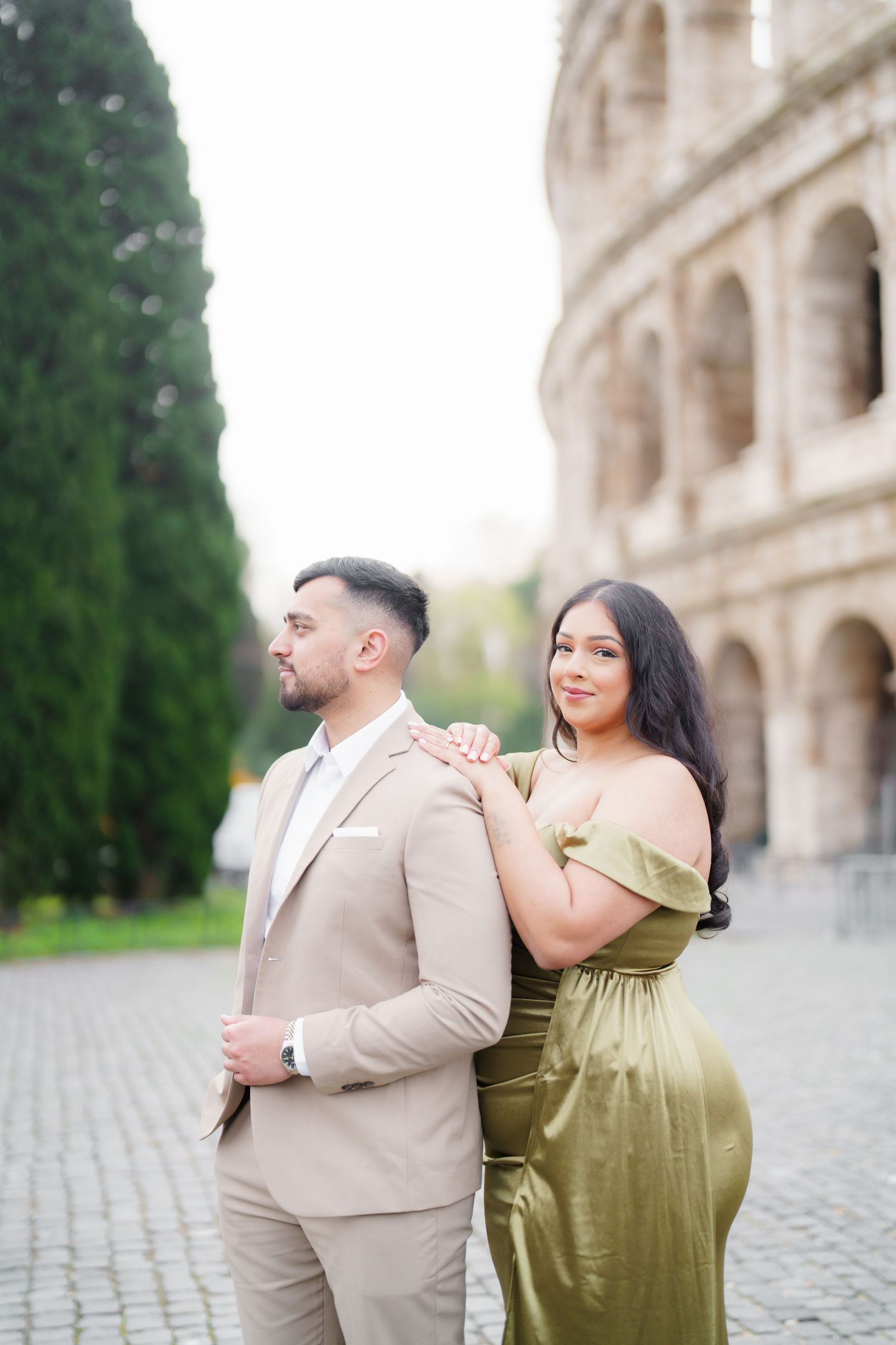 Couple posing in front of the Colosseum in Rome, man in beige suit, woman in olive green gown.