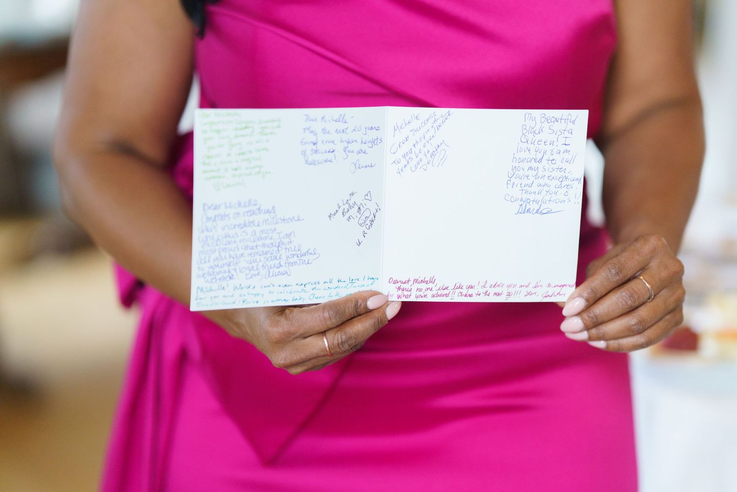 Woman in pink dress holding open greeting card covered in handwritten messages and signatures.