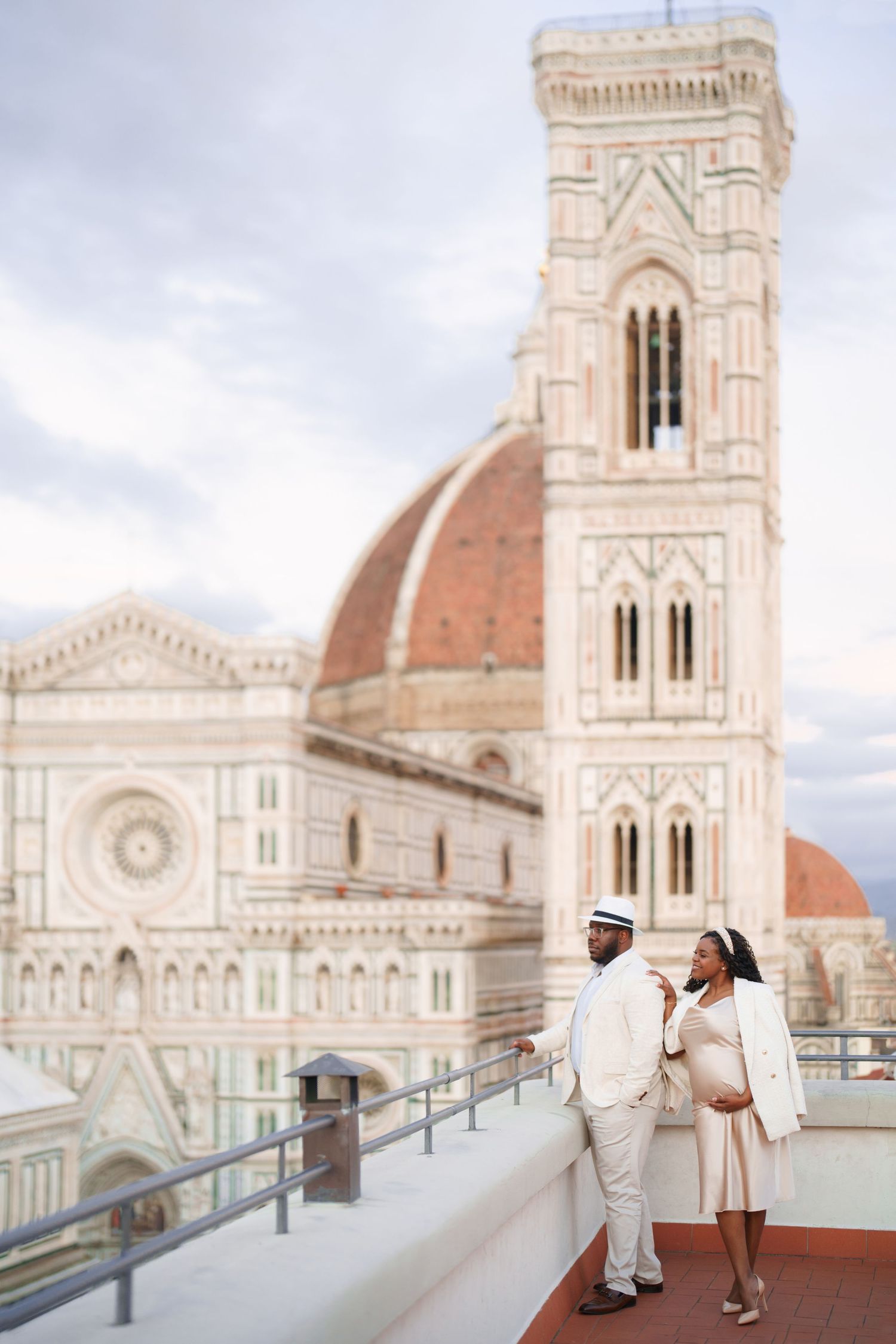 Couple in white attire on a rooftop terrace with Florence Cathedral and Giotto's Campanile backdrop.