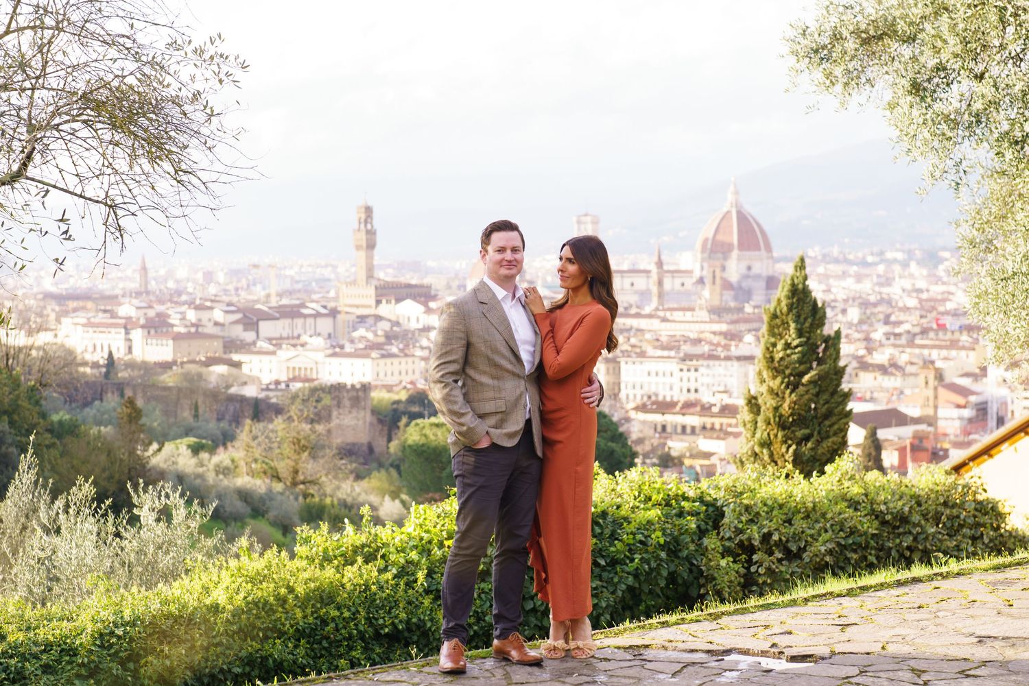 Couple embracing with Florence skyline and cathedral dome backdrop on sunny day.