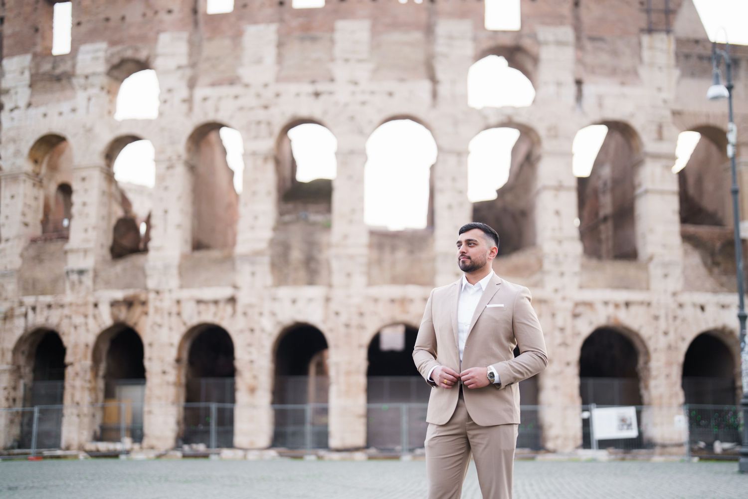 Man in beige suit posing confidently in front of the ancient Colosseum in Rome, Italy.