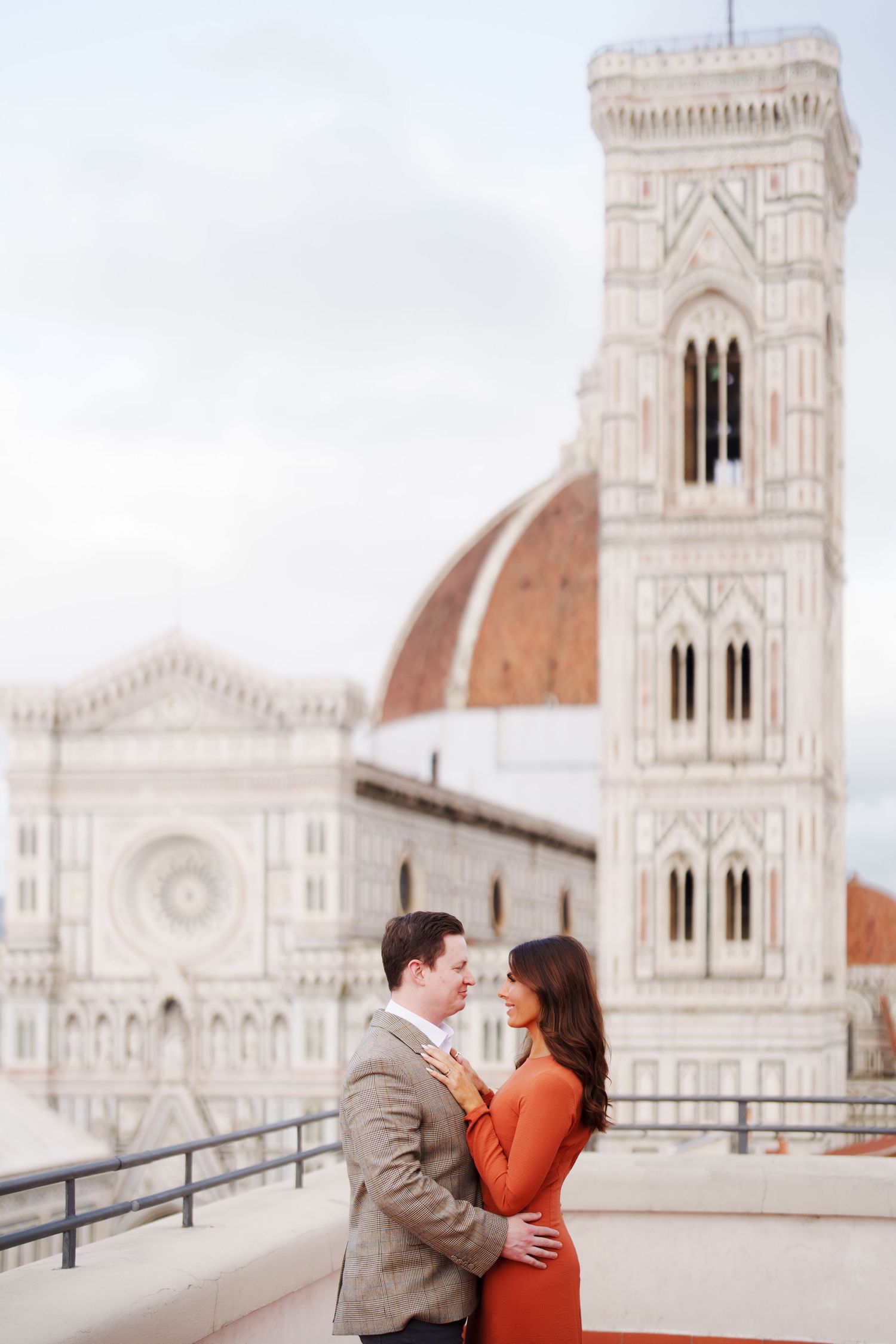 Couple embracing on a rooftop terrace with Florence Cathedral and Giotto's Campanile in the background.