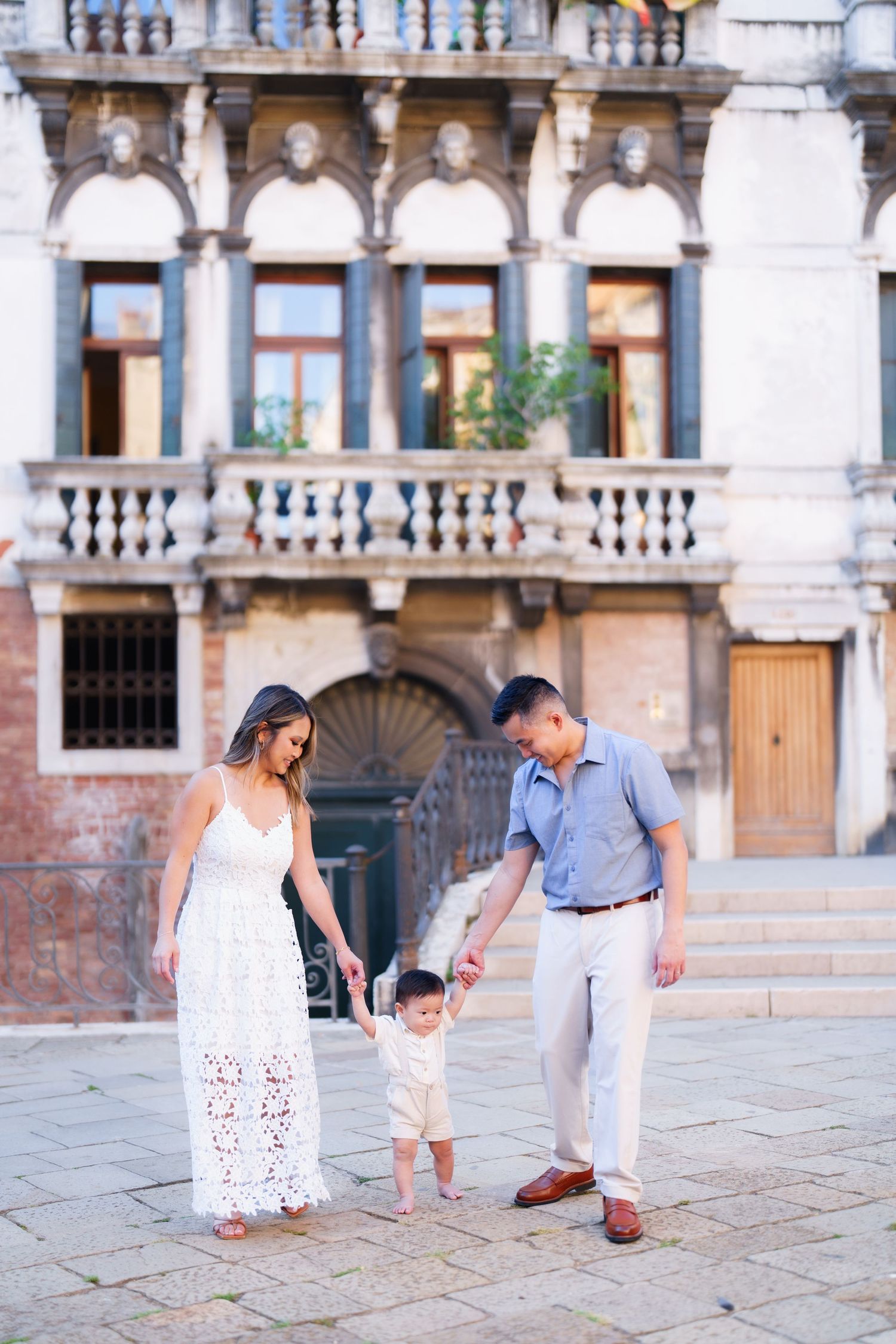 Family with toddler enjoying a sunny day in a classic Venetian square, with ornate historic architecture in the background.