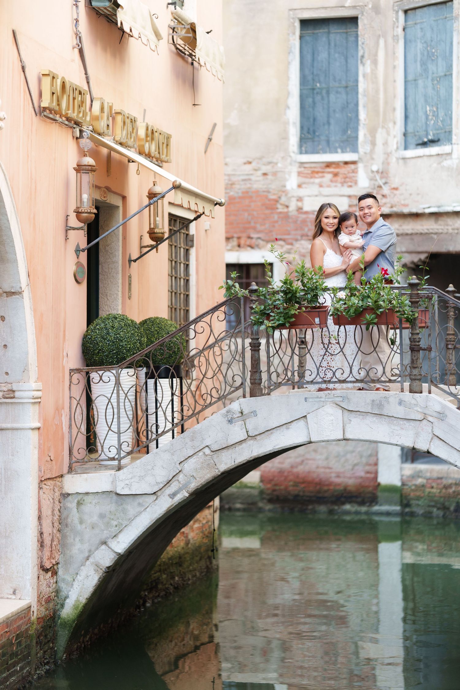 Family posing on a charming stone bridge over a Venetian canal in Venice, Italy, surrounded by historic buildings.