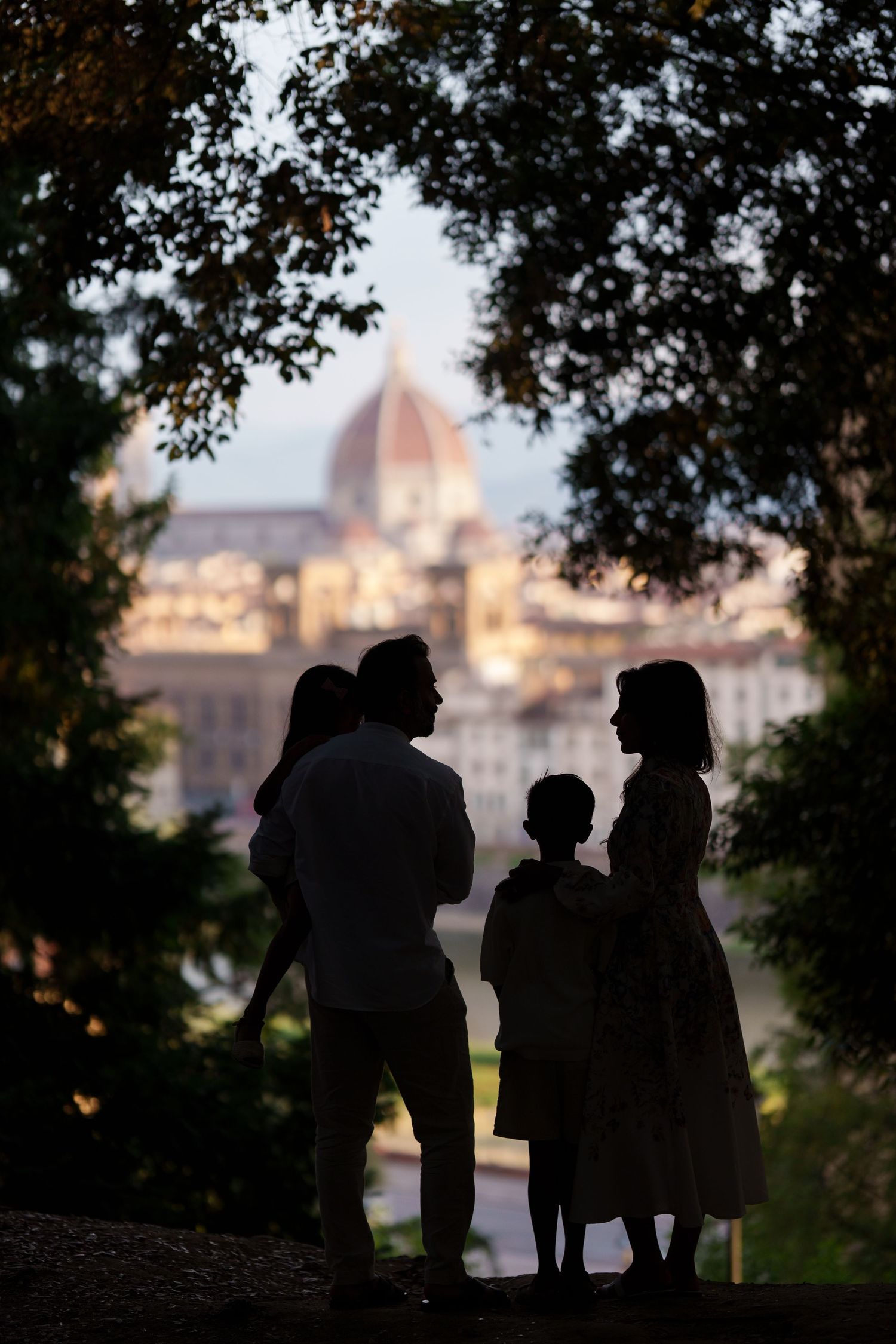 Silhouette of a family framed by trees with Florence Cathedral dome at dusk in background.