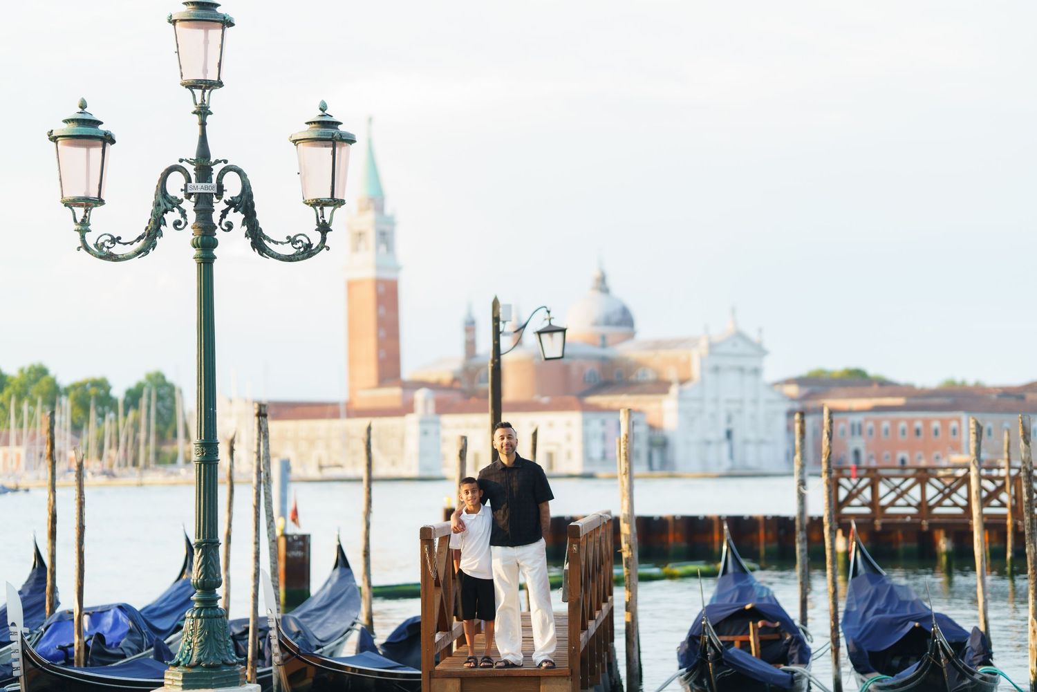 Couple standing on a dock with gondolas and San Giorgio Maggiore church in Venice, Italy backdrop.