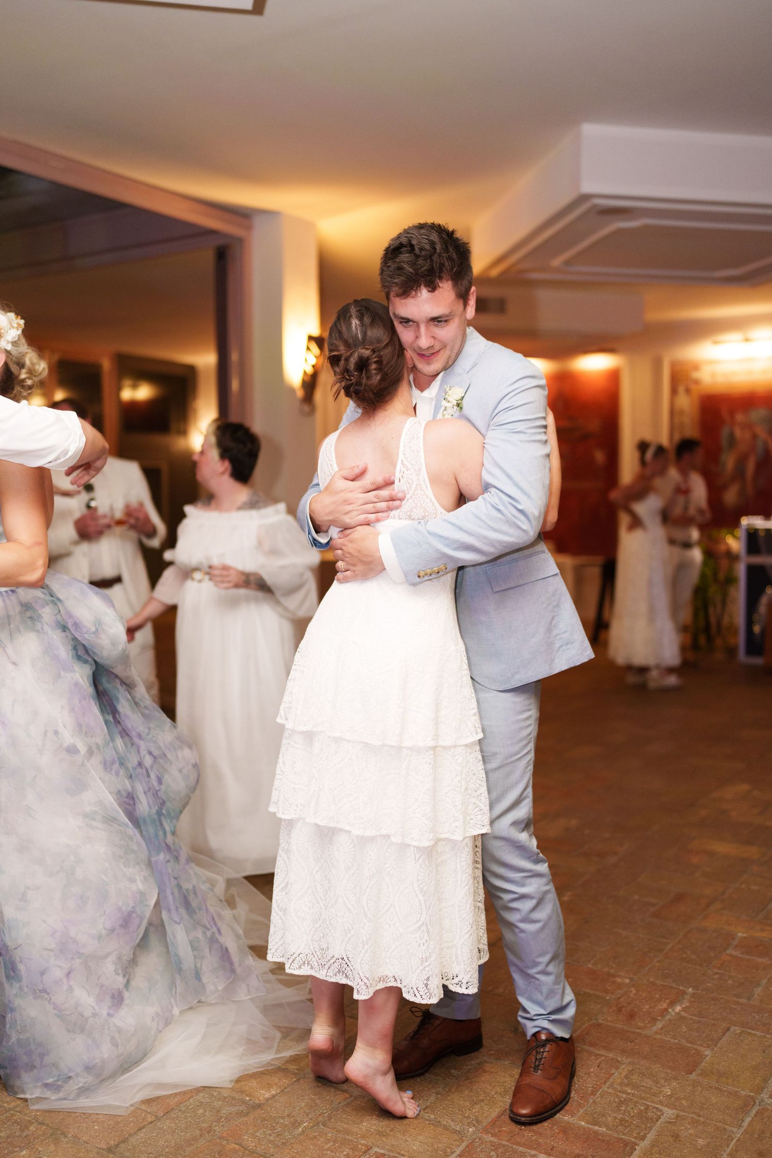 Bride and groom share their first dance at wedding reception, groom in light gray suit embracing bride in white tiered dress.