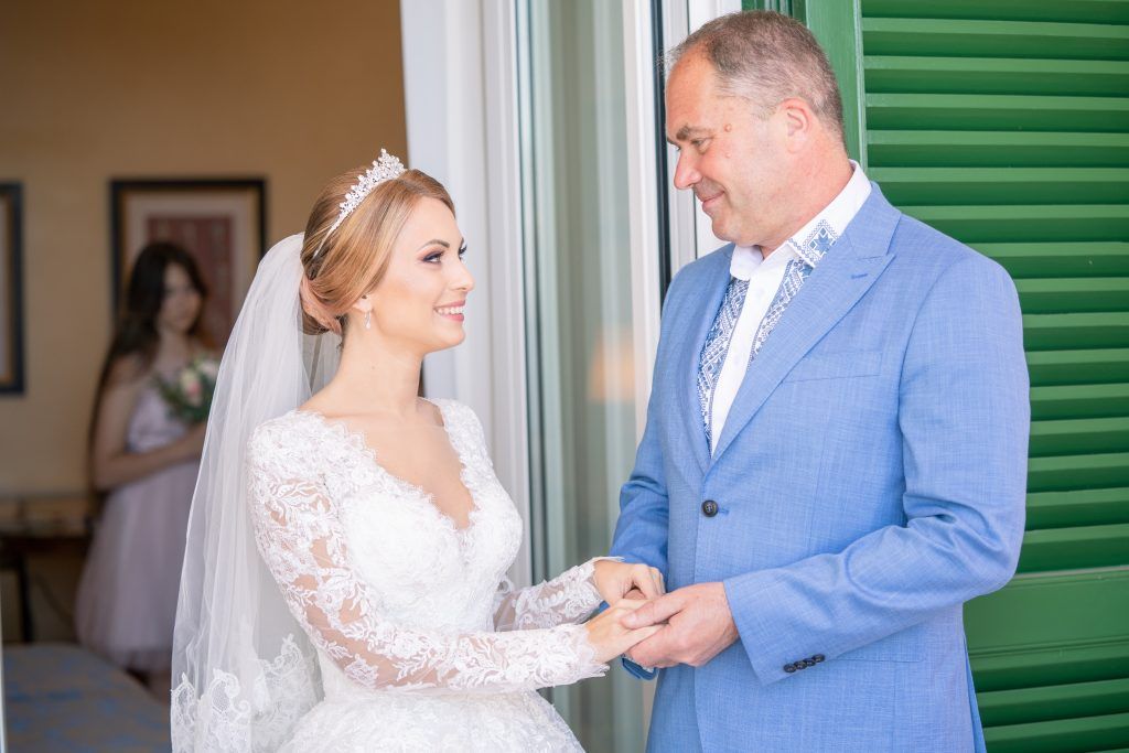 Elegant wedding couple shares intimate moments in front of green shuttered windows.