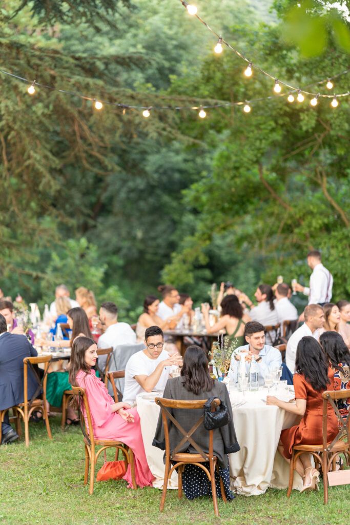 Wedding guests enjoying dinner at tables set up in a lush garden setting with string lights.