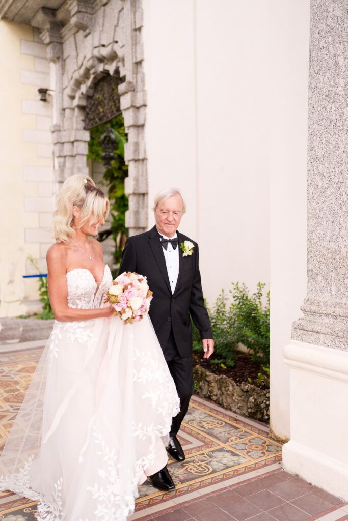 Wedding ceremony taking place in an elegant white columned corridor with arched architecture.