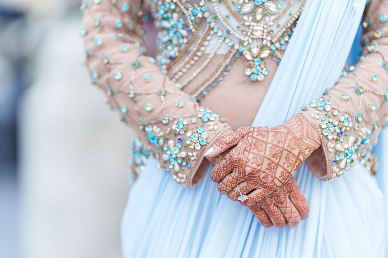 Close-up of hands with henna designs against light blue fabric with crystal embellishments.