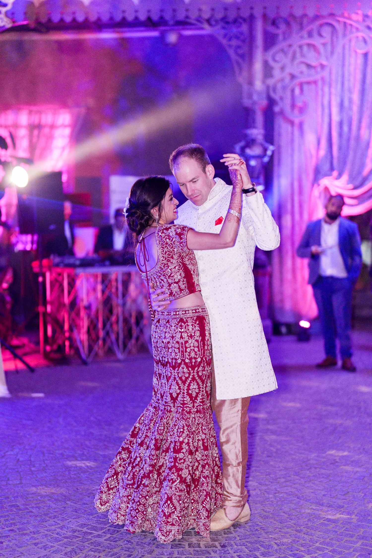 Dancers move gracefully across a cobblestone floor at an elegant reception with purple lighting.
