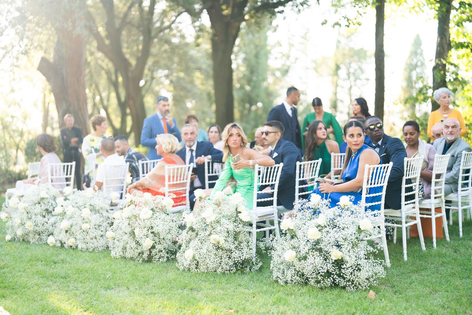 White chairs arranged in rows with floral decorations for an outdoor garden wedding.