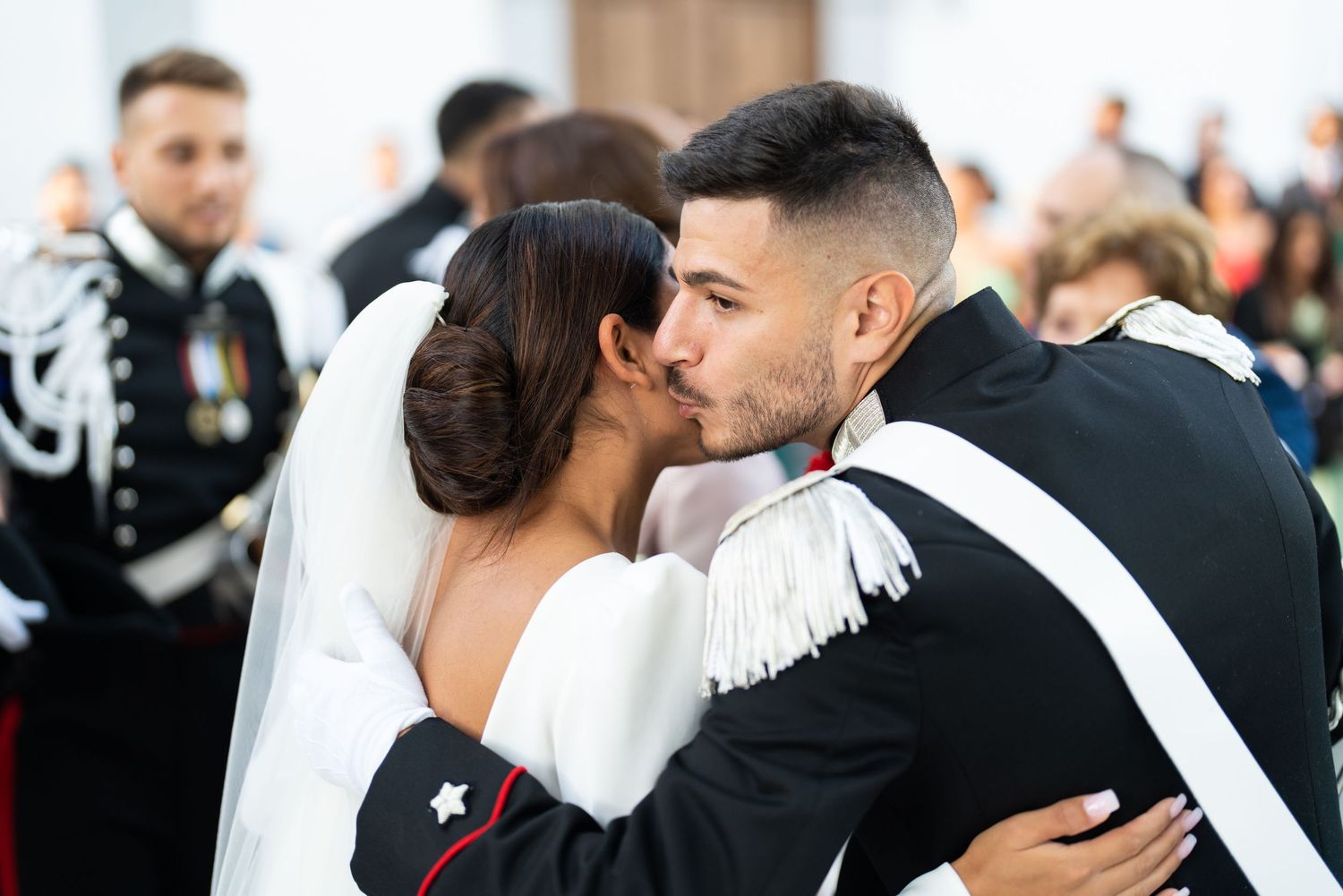 A romantic wedding kiss between a couple in formal military attire.