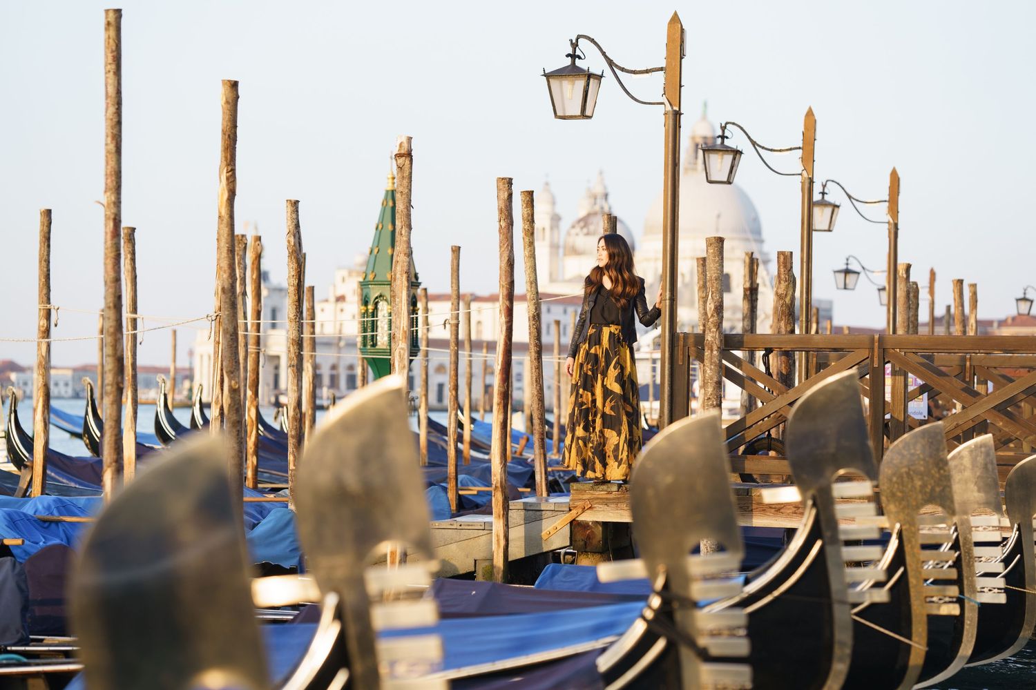 A row of traditional wooden gondola mooring poles stretches along the Venice waterfront at sunset.