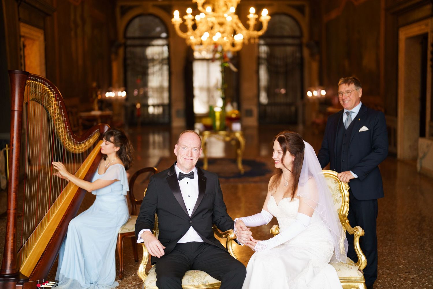 Elegant wedding reception in a grand ballroom with chandeliers and guests dancing on the wooden floor.