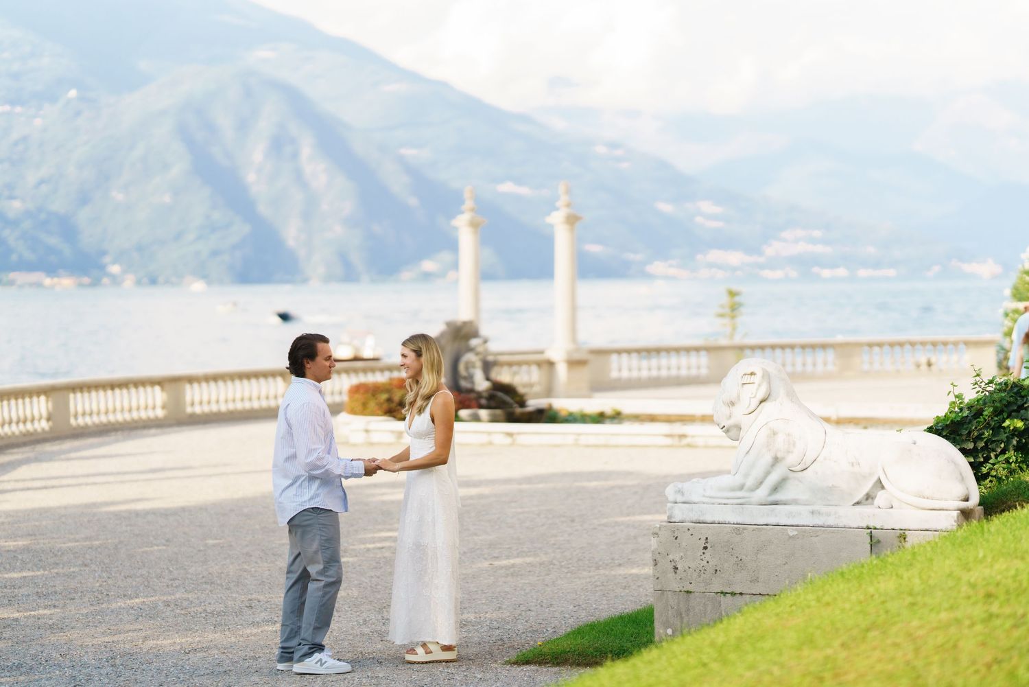A couple shares a romantic moment on a scenic overlook with mountains and water in the background.