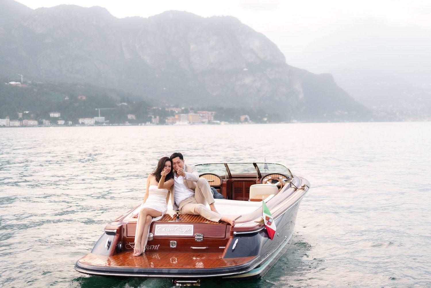 Wooden boat cruising on a scenic mountain lake with rugged peaks in the background on a misty day.