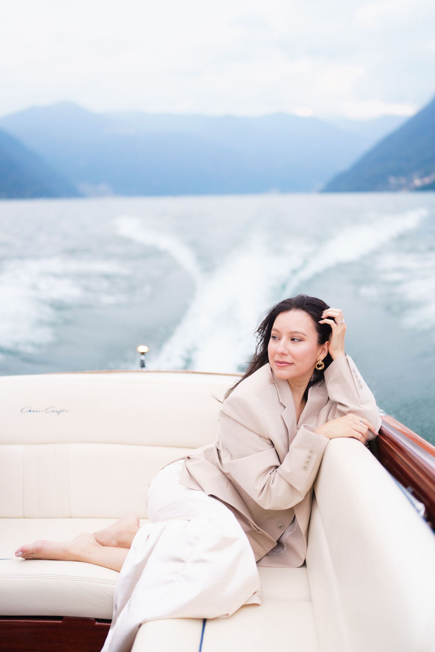 A person in beige loungewear relaxes on a white boat seat with misty mountains in the background.