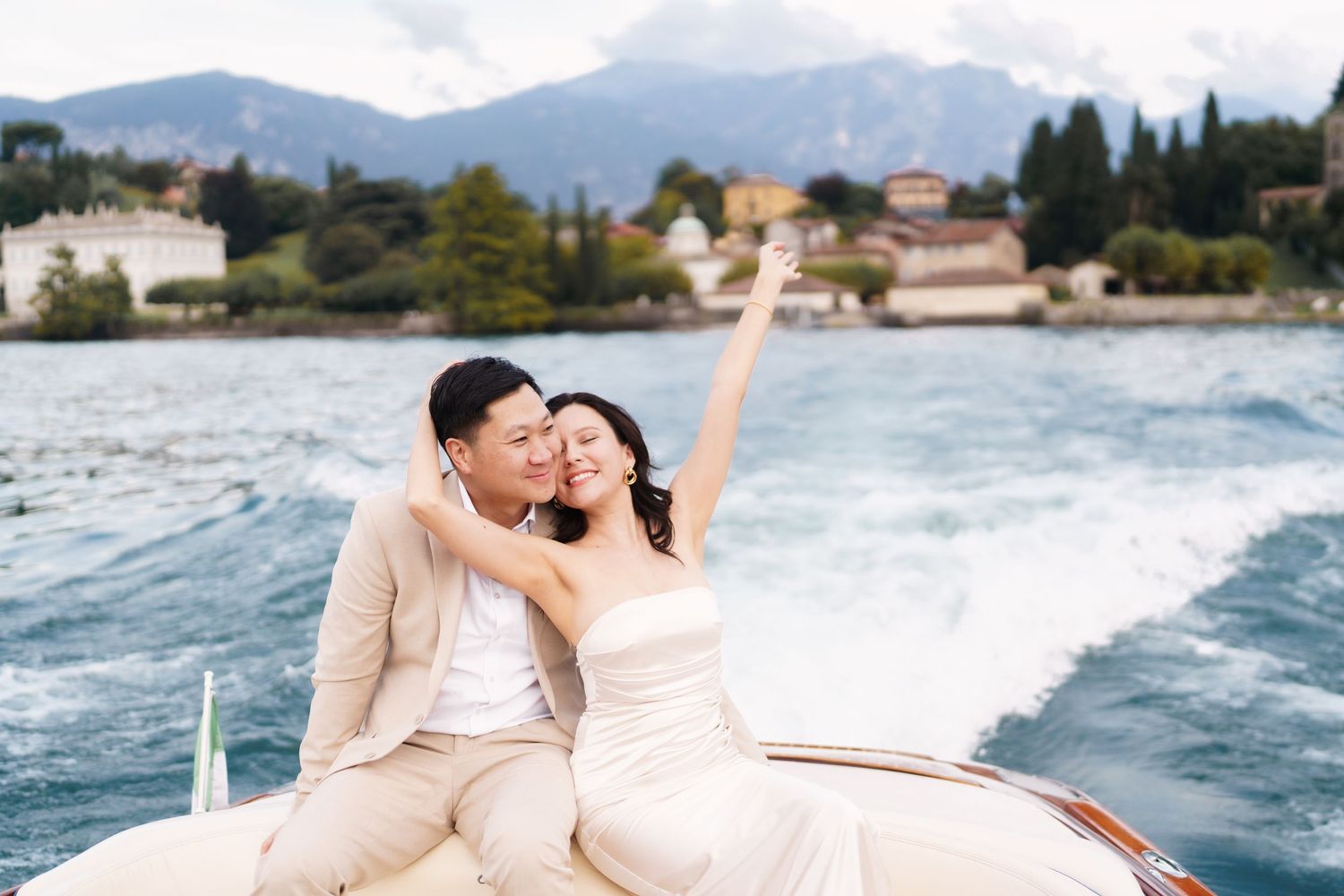 A couple shares romantic moments during a beachside photo session wearing light colored outfits against ocean waves.