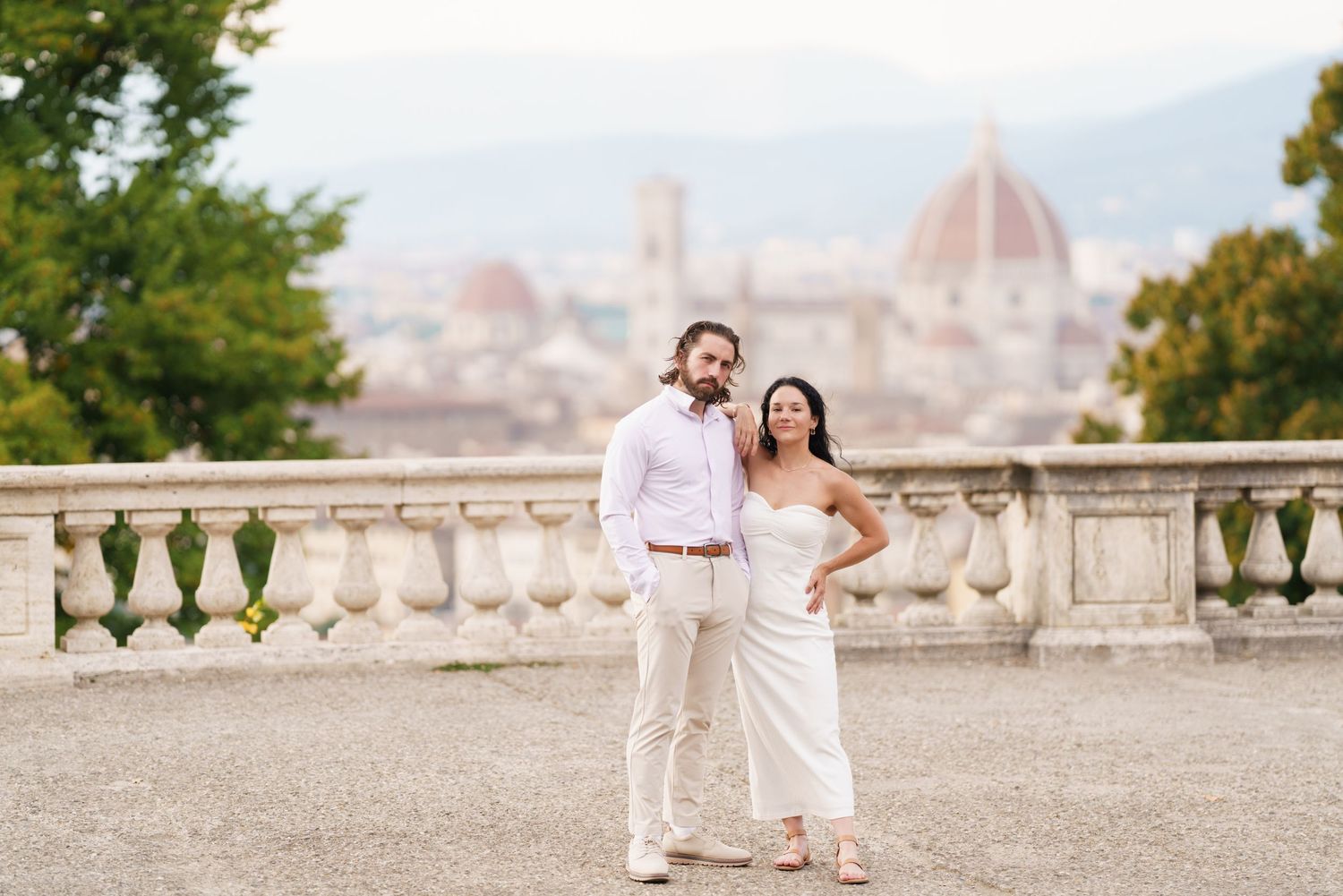 A romantic couple in white outfits share tender moments at a scenic overlook in Florence, Italy with the Duomo visible.