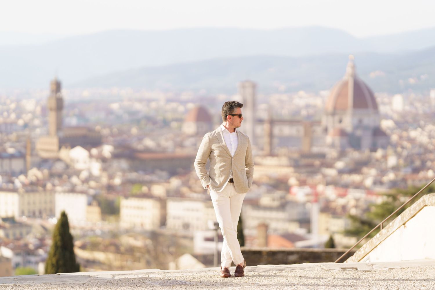 A person in light colored clothing stands overlooking the iconic Florence cityscape with the Duomo cathedral dome in the background.